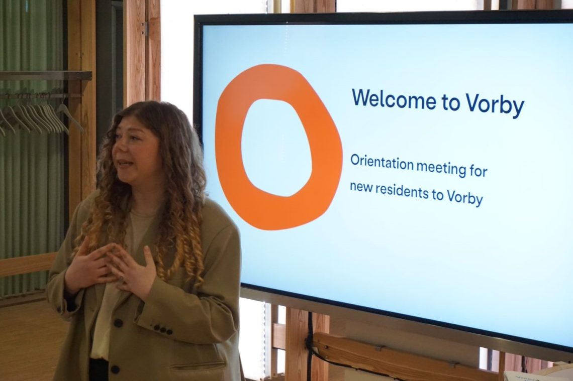 prowadząca spotkanie przed ekranem z napisem: Welcome to Vorby. Orientation meeting for new residents to Vorby"