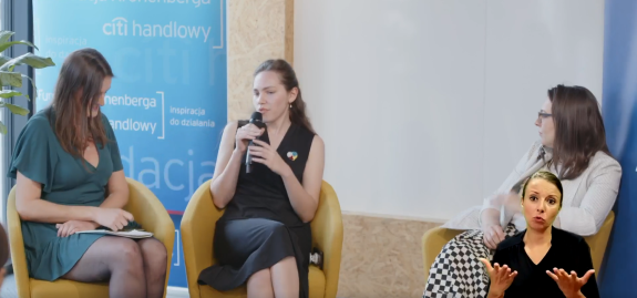 Zdjęcie przedstawia trzy kobiety prowadzące dyskusję panelową przy mikrofonie.