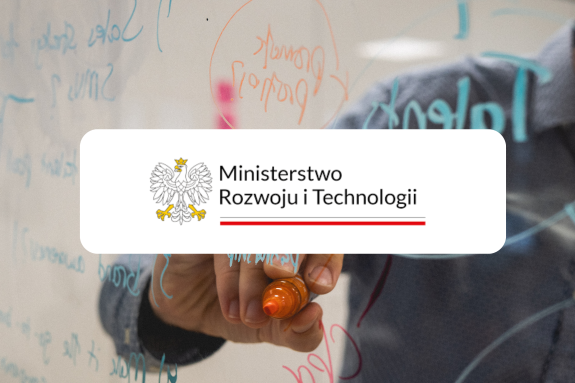 Logotyp Ministerstwa Rozwoju i Technologii. W tle sylwetka osoby rozpisującej jakiś schemat na szklanej tafli