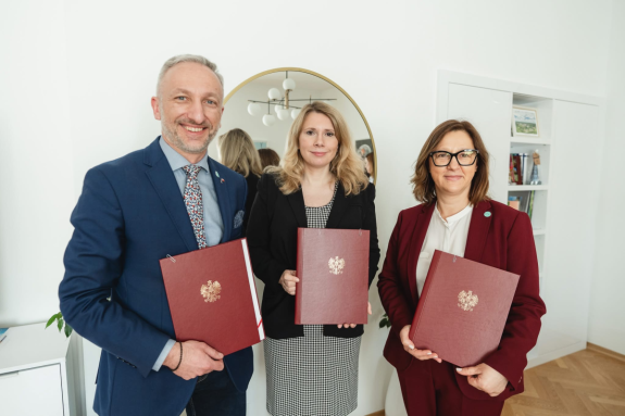 Troje uśmiechniętych ludzi trzymających umowę na projekt "Innowacje w samorządzie". Wśród nich wiceministra Monika Sikora.