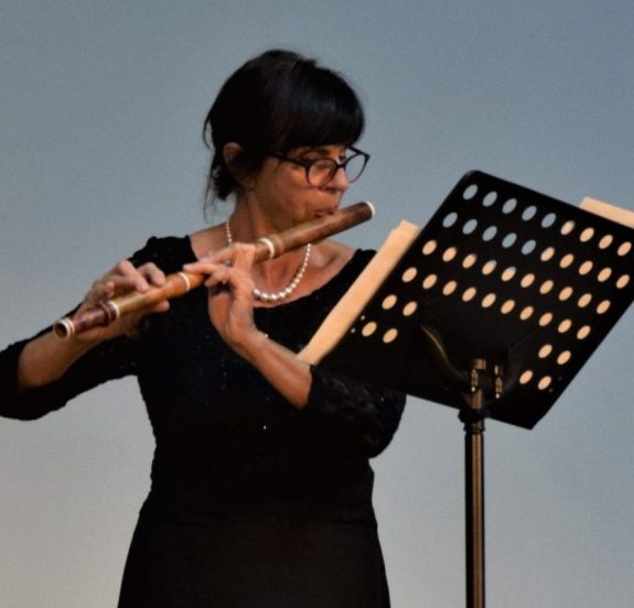 Duet muzyków, kobieta w długiej czarnej sukni gra na flecie poprzecznym wpatrzona w partyturę